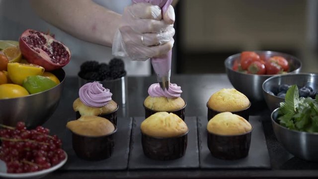 Decorating cup cake with cream. Using cooking bag, confectioner making muffins