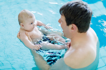 Happy middle-aged father swimming with cute adorable baby in swimming pool.