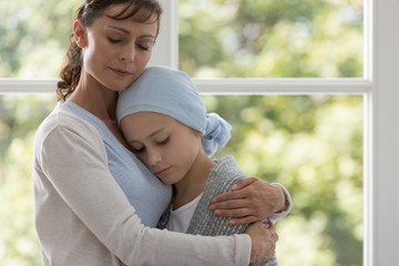 Mother hugging sick daughter with cancer wearing blue headscarf