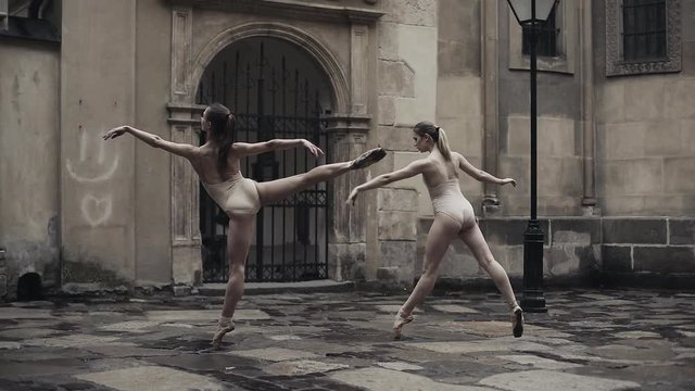 Young professional female dancers is performing acrobatic dance along the medieval street under the rain. Wet girls dancing in water drops, slow motion
