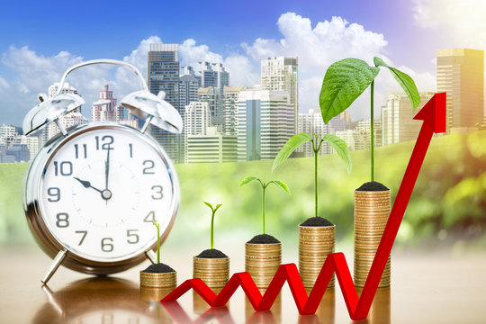 Money growing plants on money coins stack arranged as a graph with alarm clock and red arrow with blur nature and cityscape background - Powered by Adobe