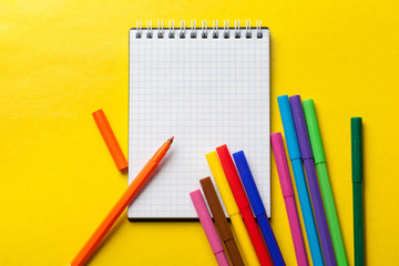 Felt-tip pens and blank notepad on bright yellow background