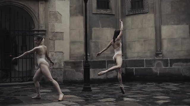 Young professional female dancers is performing acrobatic dance along the medieval street under the rain. Wet girls dancing in water drops, slow motion