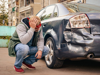 Guy sitting near the wrecked car after the accident, clutching his head.