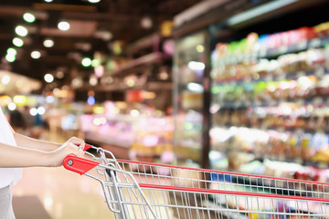 woman hold shopping cart with blur supermarket fresh product shelves background