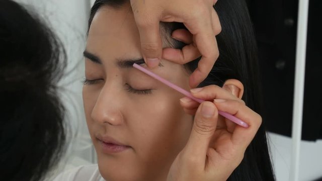 Stylist applying apply makeup on a eyebrows to the beautiful woman