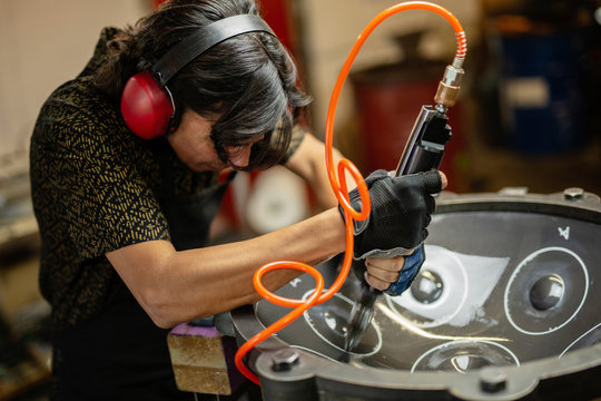 Artisan in his workshop using air hammer to construct a handpan, metal percussion instrument.