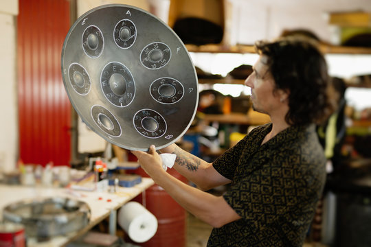 Artisan in his workshop holding the finished design of a handpan, a metal percussion instrument.