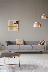 Real photo of a minimalistic living room interior with a sofa, copper table and chandelier