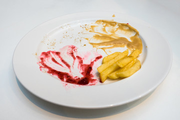 Empty dish after food, red and yellow sauce food leftovers and french fries on a white plate.