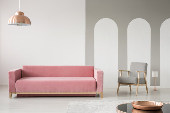 Real photo of a creative living room interior decorated with arches, pink sofa and retro armchair