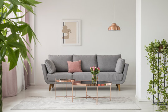 Real photo of a comfy sofa, copper coffee table and plants in a bright living room interior