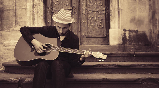 Trendy guy playing the guitar in the street. Retro styled. Music, art, creativity concept.