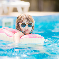 Child in swimming pool on funny inflatable donut float ring, learning how to swim.