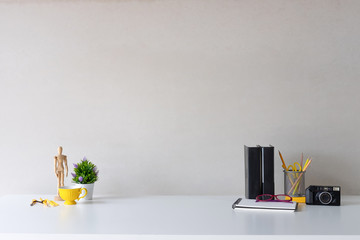 Education table with plant, cup of coffee, books, camera and jar of pencil on white table.