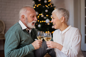 Senior couple cheering next to a beautiful decorated Christmas tree with ornaments 