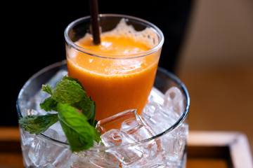 A glass of mixed orange and carrot juice in a jar of ice with mint leaves