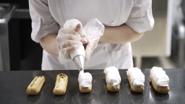 Decorating eclairs with cream. Using cooking bag, confectioner making eclairs