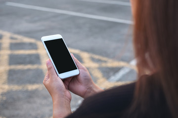 Mockup image of a woman holding white mobile phone with blank black screen with street background
