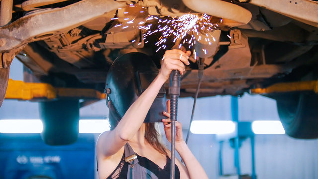 Sexy mechanic girl in a helmet repairs the car with a welding. Fire flakes