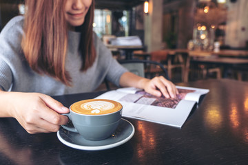 Closeup image of a beautiful asian woman reading magazine while drinking coffee in modern cafe