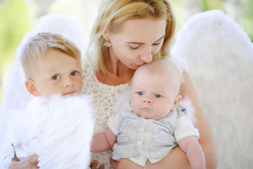 Beautiful mother and her toddler son and daughter wearing angel costumes. Cheerful moment, loving family.