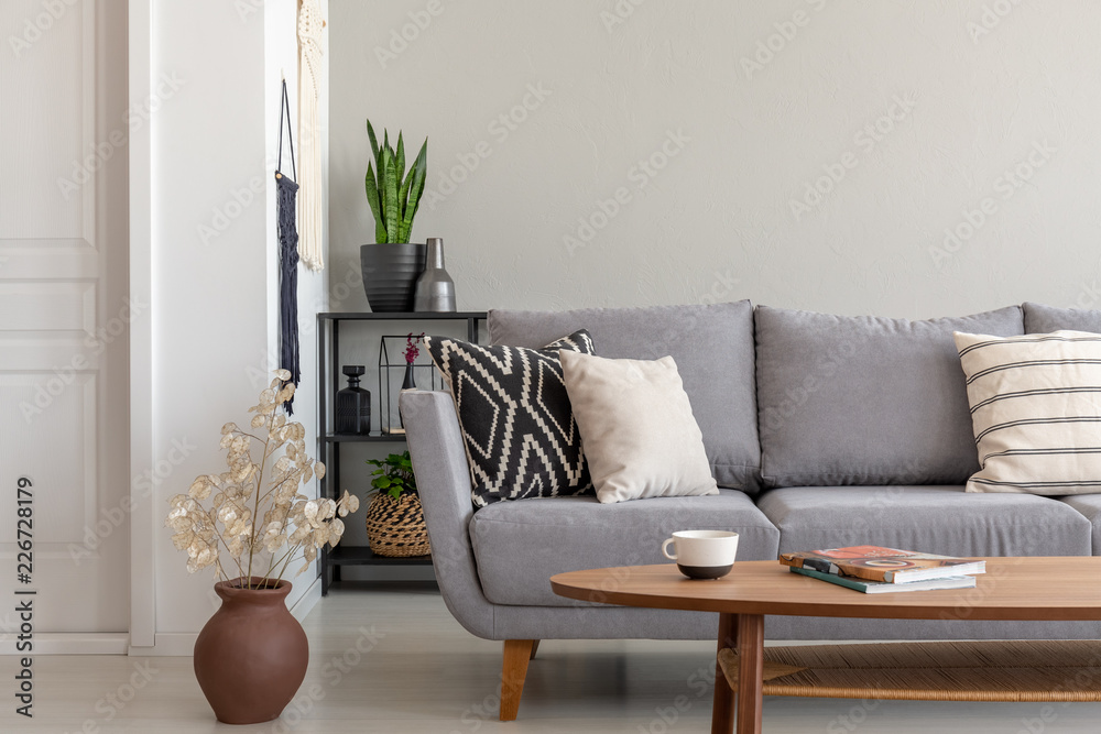 Canvas Prints Flowers next to grey couch with pillows in minimal living room interior with wooden table. Real photo