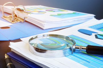 Financial audit report and magnifying glass on a desk. - obrazy, fototapety, plakaty