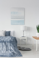 White wooden table with stylish lamp next to comfortable ned with blue pillows and duvet, real photo