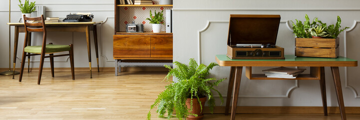 Panorama of record player on wooden table in natural home office interior with plants. Real photo