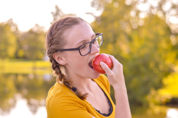 Junge Frau mit Zöpfen beißt in einen roten Apfel an einem See, Herbst, Erntezeit, gesunde...