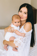 attractive young mother with her little baby boy sitting on bed at home
