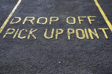 Drop off pick up point parking space sign on black asphalt tarmac in large yellow letters