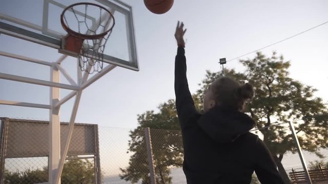 Female basketball player in morning light on professional court running with ball and thowing ball to the net. Handhelded footage. Outdoors