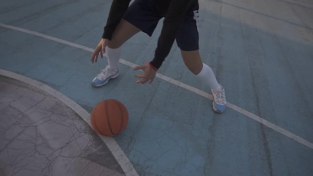 Female basketball player in shorts and white socks on professional court running with ball and successfully thowing ball to the net. Handhelded footage. Outdoors