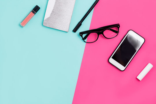 Home office desk with calligraphic pen, glasses, Notepad, smartphone and lipstick on a colorful background