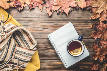 Autumn fashion seasonal concept yellow warm soft sweater Scandinavian knitted scarf cup hot black tea coffee Fall fallen maple leaves on wooden table with notebook pen. Flat lay Top view vintage style