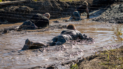 Athletes crawling under barbed wire in mud, obstacle course race 