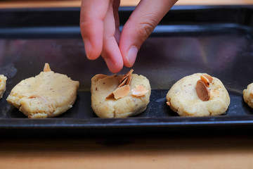 Female hand putting sliced of almond nuts on cookies over baking tray