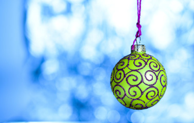 Ornament concept. Christmas decoration or toy for Christmas tree with shimmering details, copy space. Festive decoration for Christmas tree, green ball with glitter decor on blue blurred background