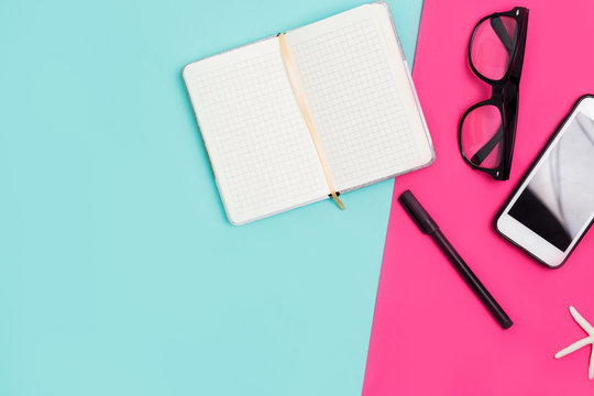Home office desk with Notepad, smartphone, glasses, pen on a colorful background, top view