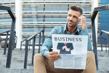 pensive smiling man holding business newspaper and looking away while sitting on stairs