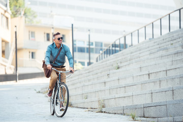 handsome middle aged businessman in sunglasses riding bike and looking away on street