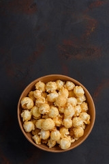 Caramel popcorn in bowl vertical on dark table with copy space