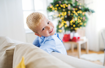 A small boy leaning on a sofa at home at Christmas time.