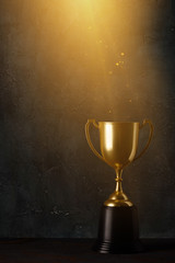 Golden trophy cup on dark table with rays of light and glitter dust dark background