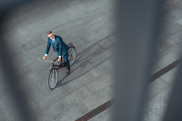 high angle view of handsome middle aged businessman in suit and eyeglasses riding bicycle