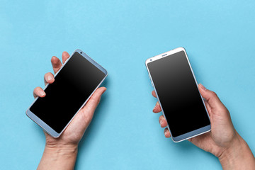 Hand of a man and woman holding a mobile on a blue background with space for text. Modern...