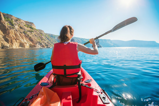 Kayaking. A Woman in a Kayak. Girl Paddling in the Calm Sea water near the rocky coast.