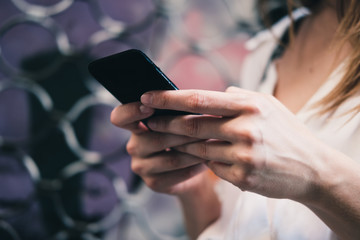Closeup of girl's hands holding smartphone and typing message. Woman using mobile device to communicate with friends. Modern world communication concept. Purple background.